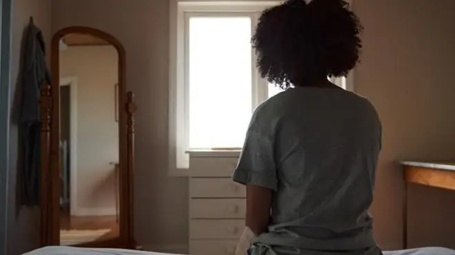 Une femme assise, enfermée seule, dans une pièce.