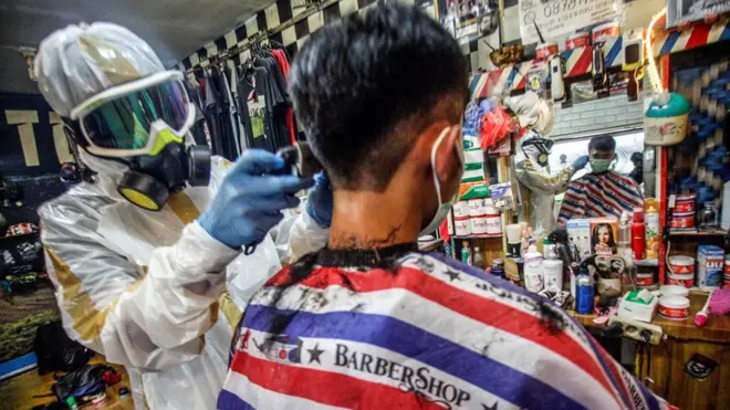 Seorang tukang cukur di Ciawi, Bogor mengenakan alat pelindung diri (APD) saat memangkas rambut pelanggan.