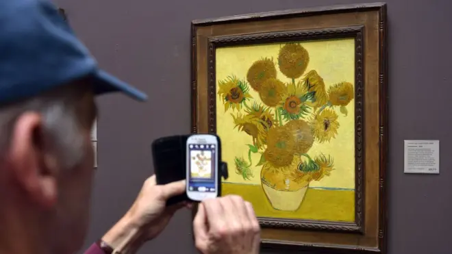 A member of the public photographing the National Gallery's version (catalogue no: NG3863) of Sunflowers by Vincent Van Gogh. The National Gallery has in the past month changed its photography policy and now allows visitors to take photographs of its permanent collection for non-commercial purposes.