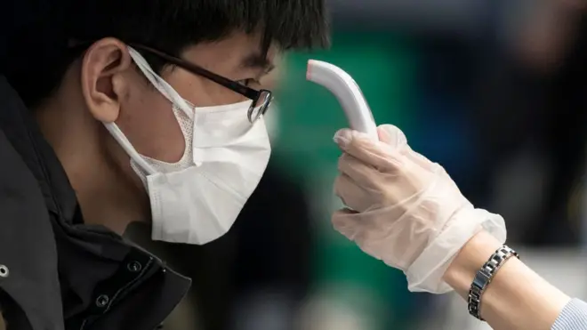 Pesin dey check di temperature of one Chinese traveller wey dey go Wuhan from Tokyo, Japan on January 31, 2020