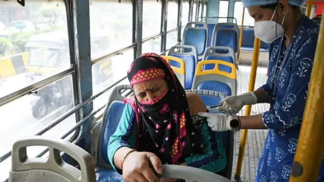 బస్సులో ప్రయాణిస్తున్న మహిళకు టీకా వేస్తున్న హెల్త్ వర్కర్