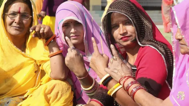 Mujeres en India muestran el dedo manchado con tinta indeleble que indica que votaron en las elecciones en Jaipur, diciembre 7, 2018