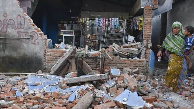 Seorang perempuan melintas dekat kios yang temboknya roboh pascagempa bumi di Dusun Lendang Bajur, Kecamatan Gunungsari, Lombok Barat, NTB, Senin (06/08).