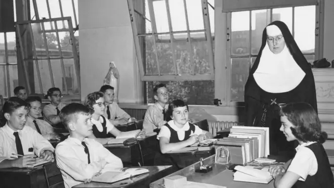 الراهبة الكاثوليكية الأخت ماري زيتا تُشاهد اجتماع الصف بينما تترأسه رئيسة الصف سوزان في مدرسة سانت ماري أوف ذا ليك، شيكاغو، إلينوي، حوالي عام 1960.