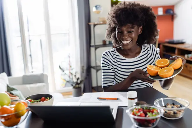 Une nutritionniste joyeuse et diversifiée montre à sa cliente, lors d'un rendez-vous virtuel, des fruits et légumes sains, des compléments alimentaires et des suppléments vitaminiques destinés à la santé et à l'alimentation.