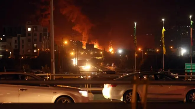 People drive as fire and smoke rise from an oil warehouse in Tehran, Iran, on 15 June 2024