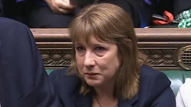 Rachel Reeve with tears visible on her cheeks sits in the House of commons - she has shoulder-length brown hair, wearing a dark blazer over a white blouse. Other members are visible in the background, some holding documents or electronic devices, in a formal parliamentary setting.