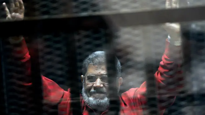 Mohammed Morsi raises his hands inside a cage in a makeshift courtroom at the police academy in Cairo, Egypt (21 June 2015)