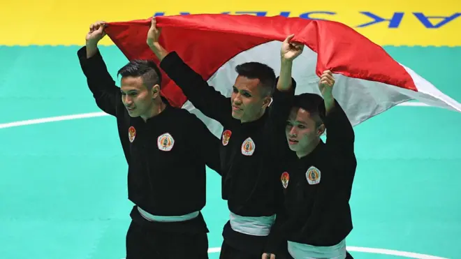 Tim silat Indonesia peraih medali emas Nunu Nugraha (tengah), Asep Yuldan Sani (kiri) dan Anggi Faisal Mubarok (kanan) merayakan kemenangan dengan membentangkan bendera merah putih usai meraih medali emas dalam final beregu putra pencak silat seni Asian Games 2018 di Padepokan Pencak Silat Taman Mini Indonesia Indah (TMII), Jakarta, Senin (27/8).
