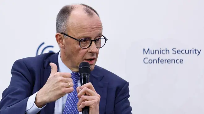 El canciller alemán, Friedrich Merz, habla y sostiene un micrófono.