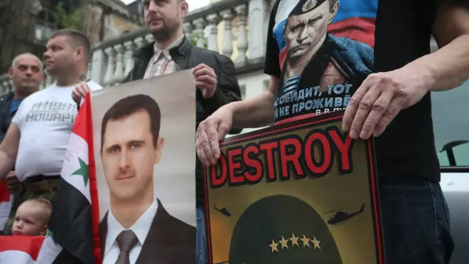 Pemrotes membawa potret presiden Suriah dan presiden Rusia dalam demonstrasi menentang serangan terhadap Suriah di Beograd.