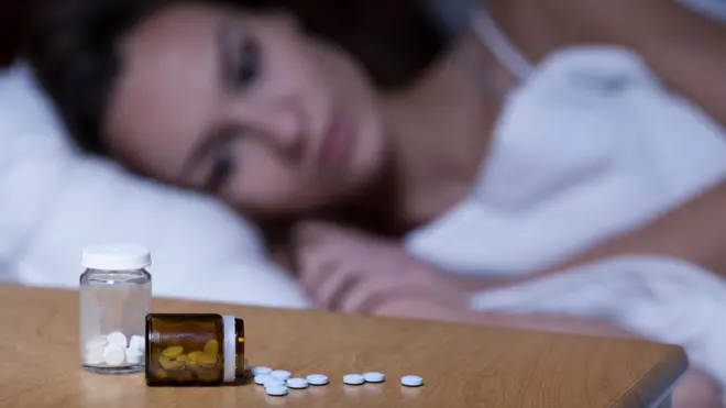 Mujer en la cama con unas píldoras para el sueño en la mesabetboo app baixarnoche