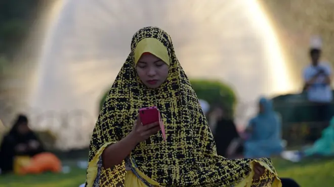 In Manila, a woman checks her phone during a quiet moment before the prayer service