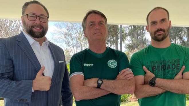 Jason Miller, Jair Bolsonaro e Eduardo Bolsonaro posam para fotojogos para ganhar dinheiro no pagbankárea externa, com árvores atrás durante o dia