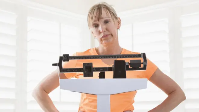 Un mujer mira su peso en una báscula