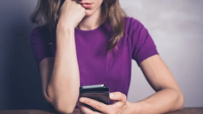 Mujer esperando con el celular en la mano.