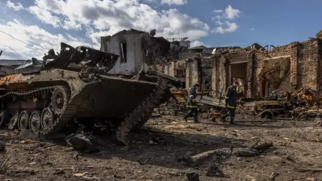 เจ้าหน้าที่กู้ภัยยูเครนเดินผ่านรถถังรัสเซียที่ถูกโจมตีเสียหายในแคว้นซูมี ในภาคตะวันออกเฉียงเหนือของยูเครน