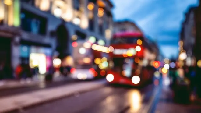 A bus approaches a stop on a London street at night