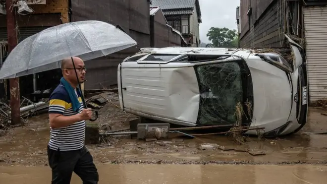 A man walks past an overnturned car