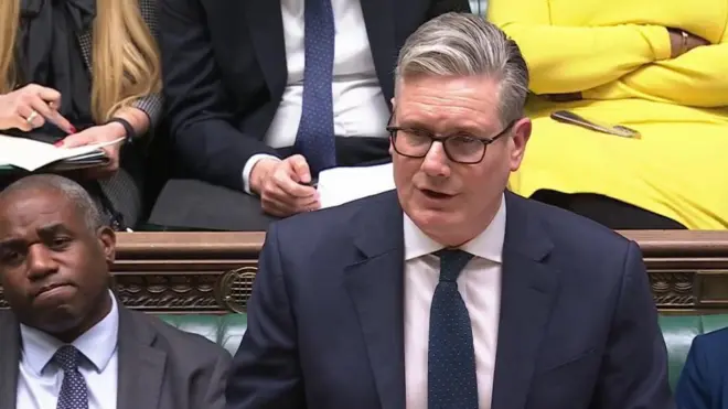 英下院の緑色の背もたれのベンチを背に、答弁するスーツ姿のスターマー英首相