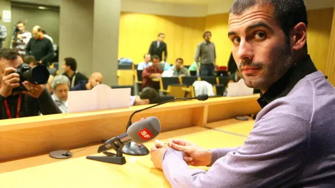 Pep Guardiola looks back at the camera in a press conference during his time at Barcelona