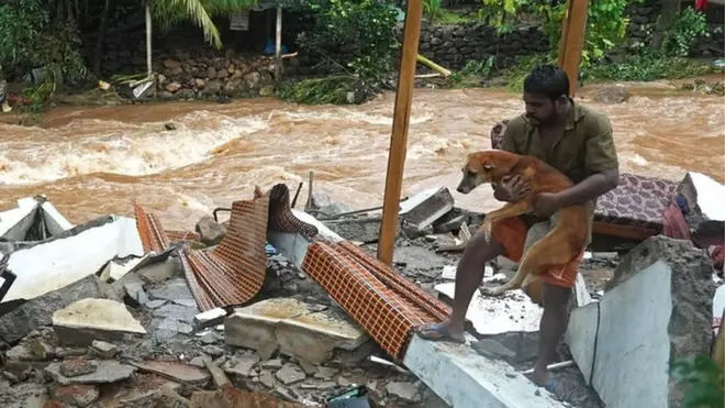 A resident carries a dog amid debris of his damaged house after flash floods caused by heavy rains at Thodupuzha in India's Kerala state, 16 October 2021