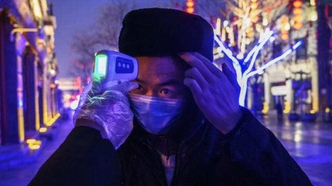 Un trabajador chino con una mascarilla registra la temperatura de un colega en Pekín, 12 de febrero, 2020