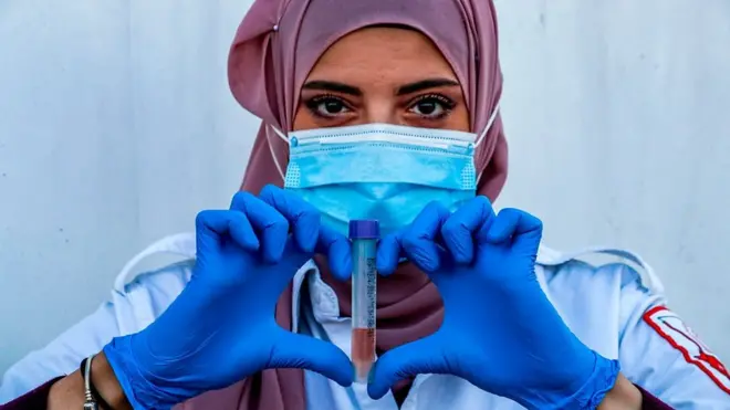 صورة محجبة مع عينة من شخص وتقوم بعمل إشارة "قلب" بأصابعها