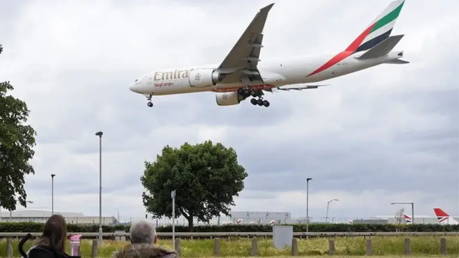 شخصان يشاهدان هبوط طائرة تابعة لشركة طيران الإمارات
