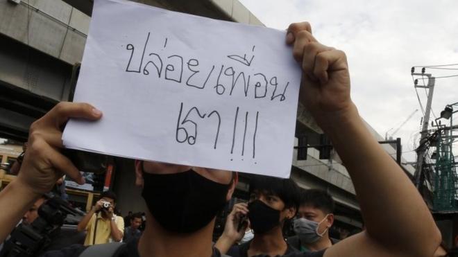 Pro-democracy protester holds a placard with a message "Free our friends" as they gather for an anti-government protest at Kaset Intersection in Bangkok,