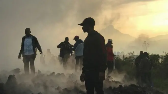 Residents walk near destroyed homes with the smouldering lava deposited by the eruption of Mount Nyiragongo volcano near Goma, in the Democratic Republic of Congo May 23, 2021