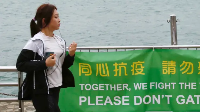 香港九龙尖沙咀一位正在跑步女士经过一面“同心抗疫请勿聚集”横幅（2/4/2020）
