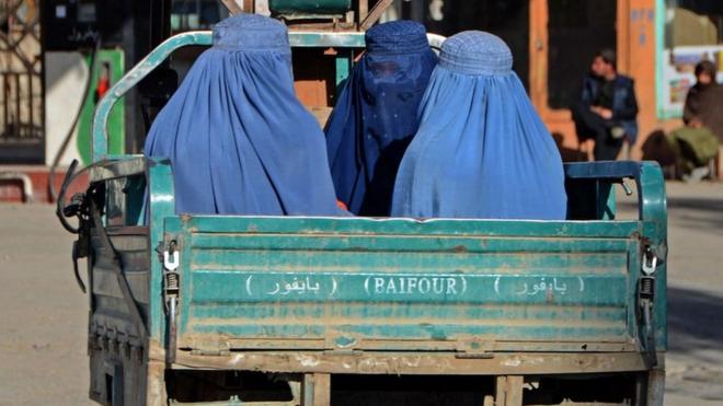 Burqa-clad women travel in a vehicle along a street in Kandahar on 18 December