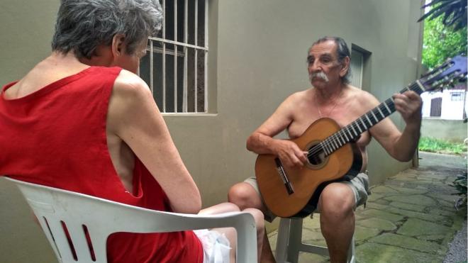 Imagem mostra o músico Lúcio Yanel tocando violão para a mulher, Sueli, que tem Alzheimer