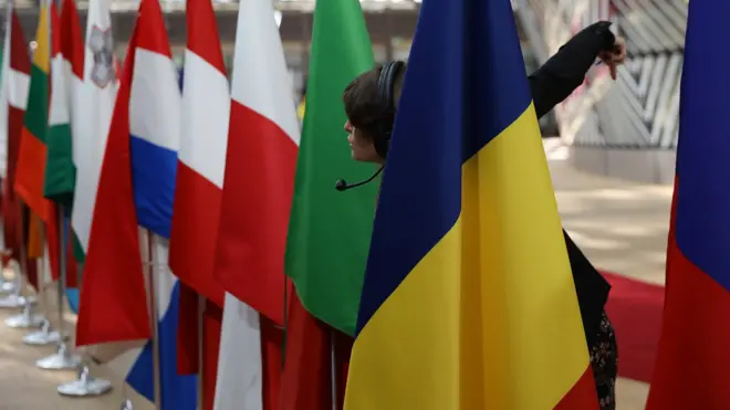 A worker leans through flags to direct people as EU leaders arrive at the Council of the European Union ahead of an EU Council meeting on April 29, 2017 in Brussels