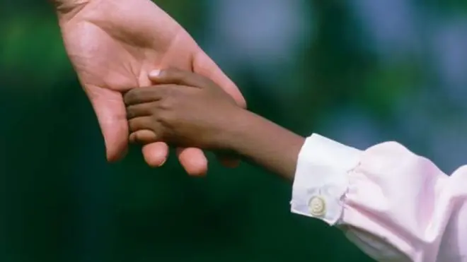 አንድ ጥቁር ህፃን እጅ የያዘ ፈረንጅ