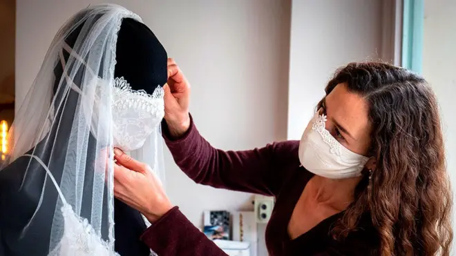 Desainer gaun pengantin dan pakaian malam Friederike Jorzig menyesuaikan manekin yang mengenakan gaun pengantin dengan masker yang serasi di tokonya, Chiton, di Berlin. Semua acara, termasuk pernikahan, telah dibatalkan di Jerman, sehingga perancang telah beralih ke membuat masker wajah modis di studionya.