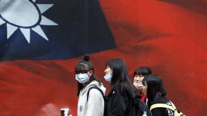 戴着口罩的台湾人走过中华民国国旗（2021年4月11日资料照片）