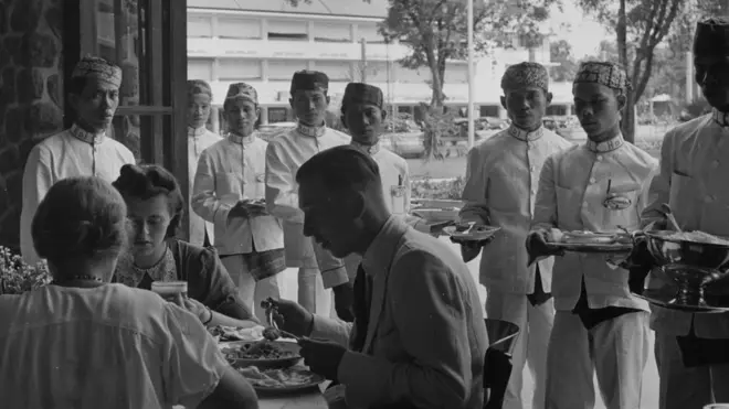 Jawa, sekitar tahun 1940: orang-orang Belanda bersantap di meja makan dengan para pramusaji di belakangnya.