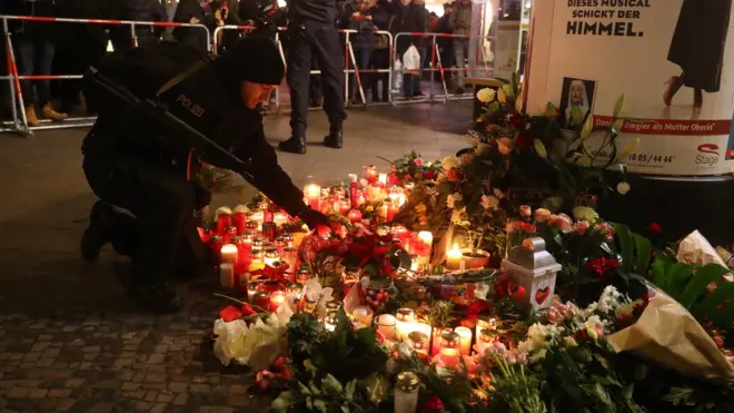 Seorang polisi menempatkan lilin di pintu masuk pasar Natal di Breitscheidplatz, Berlin, pada Selasa (20/12).