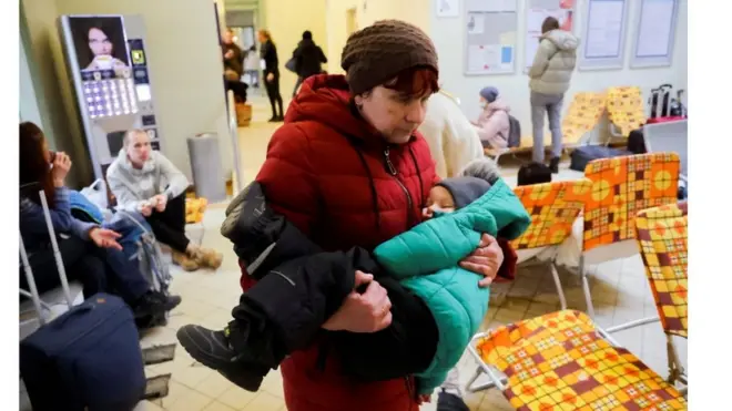 แม่ชาวยูเครนอุ้มลูกเดินหลังมาถึงสถานีรถไฟแห่งหนึ่งในโปแลนด์ซึ่งกลายเป็นศูนย์รับผู้อพยพ