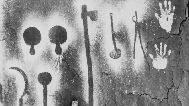 A mother and child in front of a traditional wall painting in their home in Gujarat, 1987. They were made by placing a hand or a tool against the wall and and blowing a solution of jowar (sorghum, a local millet) paste onto it, thereby creating an outline of the subject