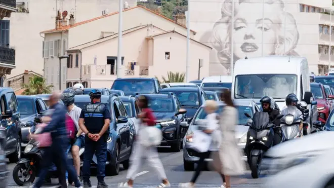 Полицейский регулирует движение, пока люди проходят мимо, а машины ждут на дороге. На здании на заднем плане изображена Мэрилин Монро.