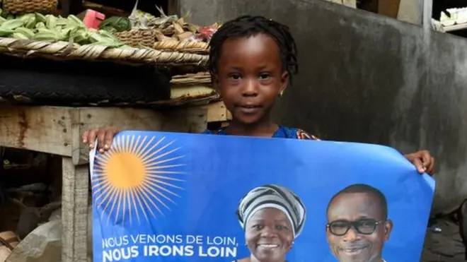 A child holds a campaign poster with photographs of incumbent Benin President Patrice Talon (R on poster) and running mate Mariam Talata (L on poster) at the market in Cotonou on April 8, 2021.