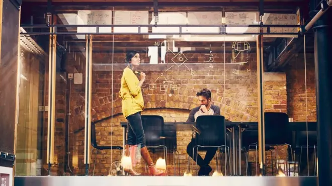 Unas personas trabajando en una oficina con pared de vidrio