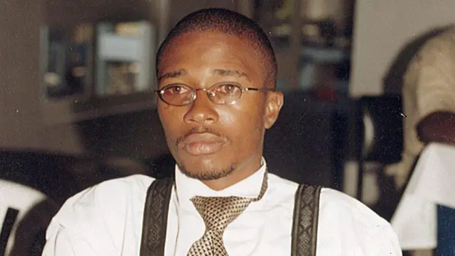 Floribert Bwana Chui Bin Kositi yambaye indorerwamo n'ishati y'umweru iriho imirongo ibiri y'ikigina ku mpande zombi, na karuvati ijya kuba ikigina