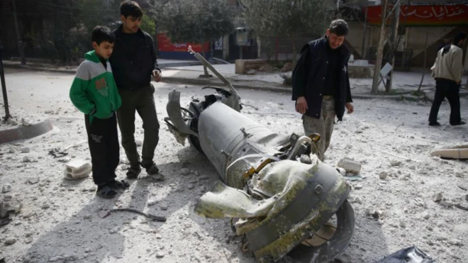 ชาวบ้านในเมืองดูมาของเขตโกตาตะวันออก ยืนดูซากจรวดที่กองทัพรัฐบาลซีเรียยิงโจมตีเข้ามา