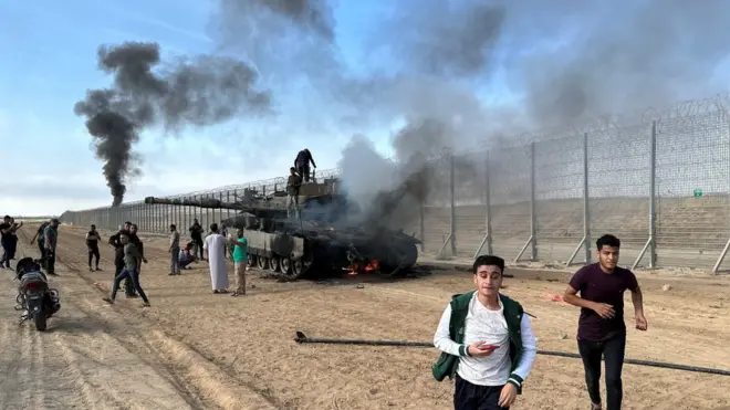 Palestinians gathered near an Israeli tank that was set alight on the Israel-Gaza perimeter fence