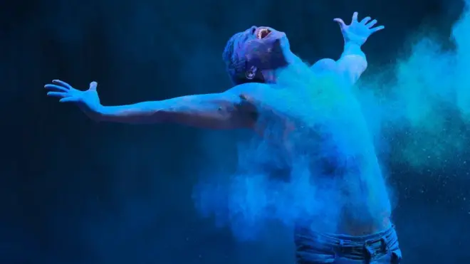 Un homme qui étend les bras est couvert de poudre bleue