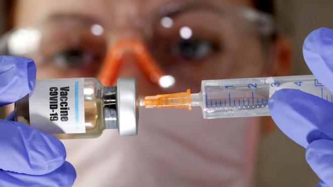 A woman holds a small bottle labelled with a "Vaccine COVID-19" sticker and a medical syringe in an illustration photo taken April 10, 2020.